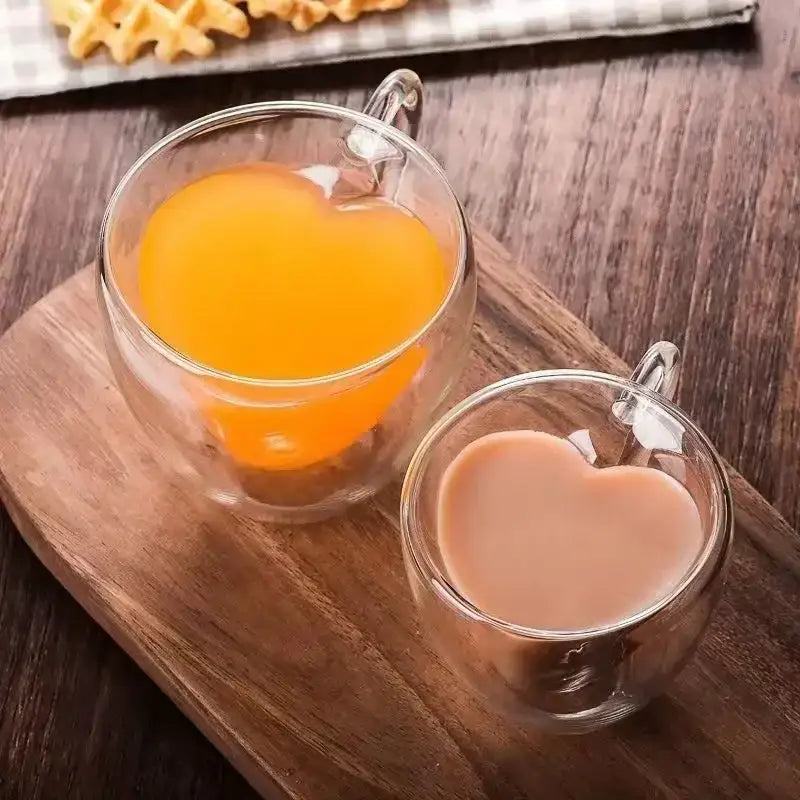 Two clear double wall glass mugs with heart shaped interiors filled with orange and light brown beverages