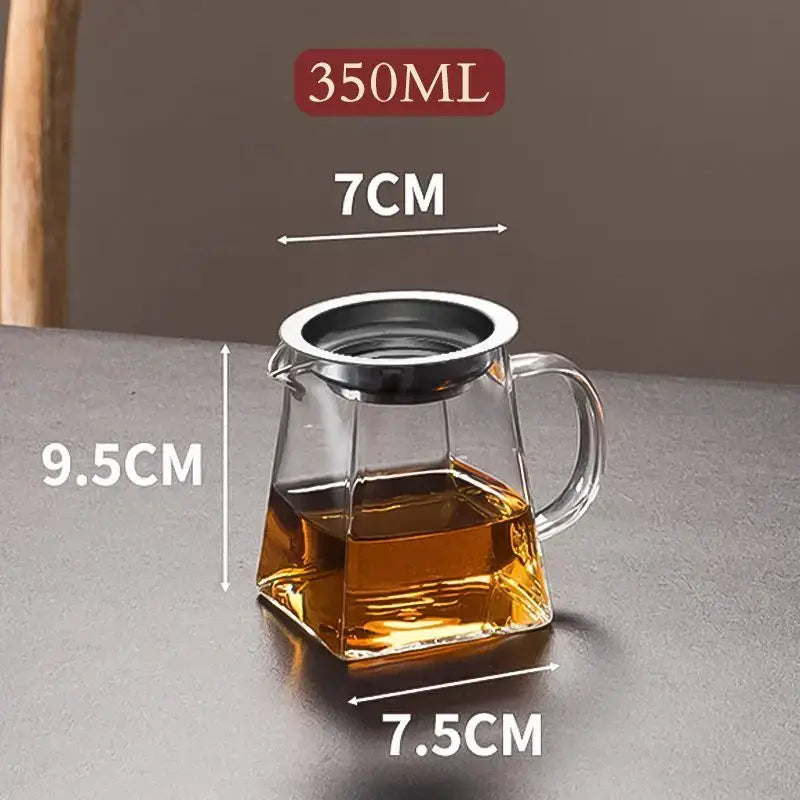 Clear glass kung fu tea set fair cup with silver metal infuser lid and handle filled with amber tea on square base