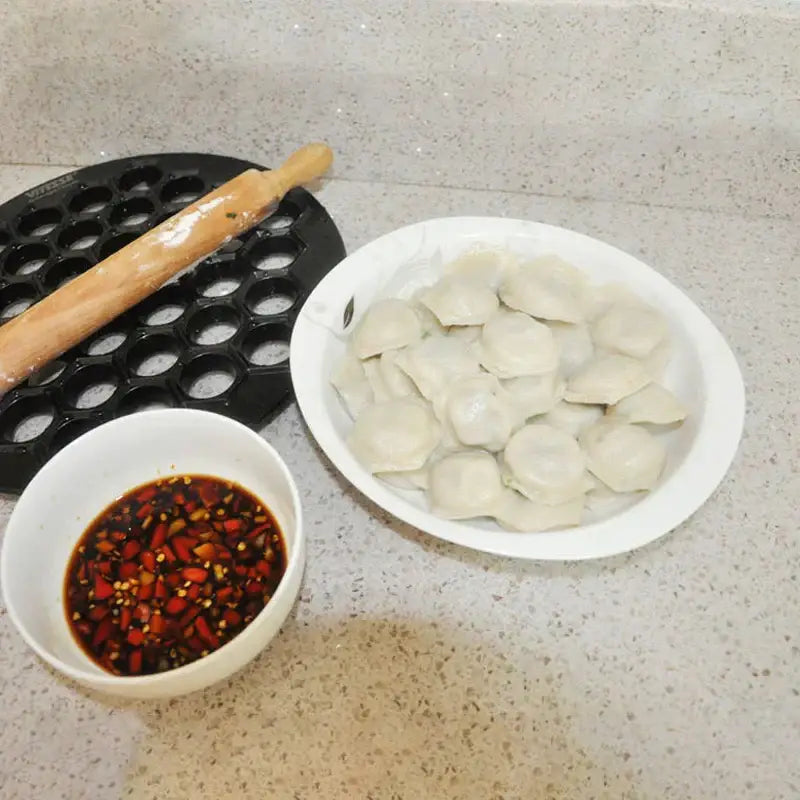 White ceramic plate holding uncooked dumplings with pleated edges made using a hexagonal black aluminum dumpling maker mold
