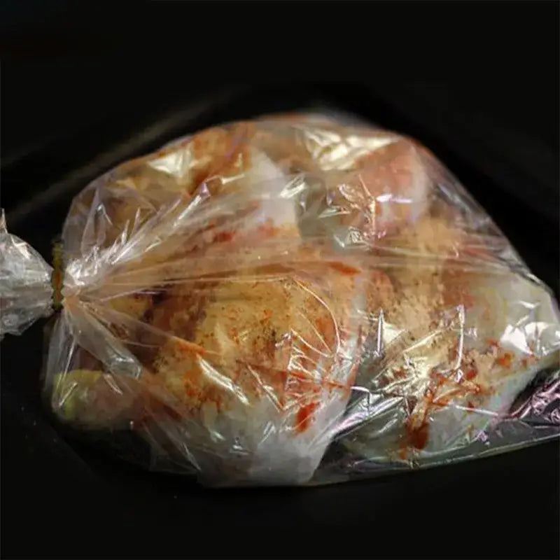 A clear plastic high temp baking bag filled with seasoned chicken from a 20 piece kitchen tool set