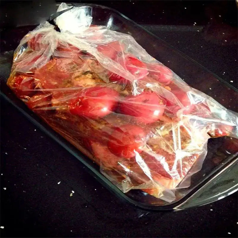 A clear plastic high temp baking bag filled with marinated meat and tomatoes from a 20 piece kitchen tool set