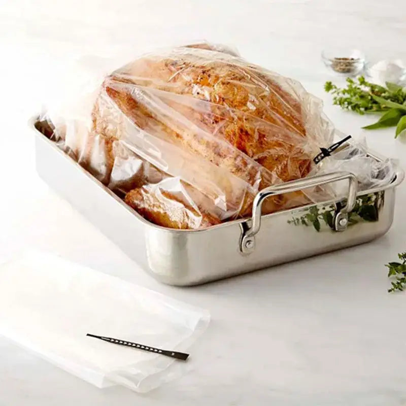 A roasted turkey in a clear baking bag inside a stainless steel pan with handles from a high temp baking tool set