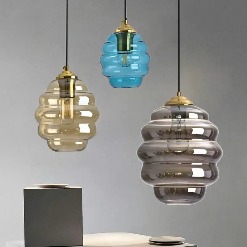 Three honeycomb-shaped glass pendant lights with brass accents in amber blue and gray colorful glass decorbites ball design