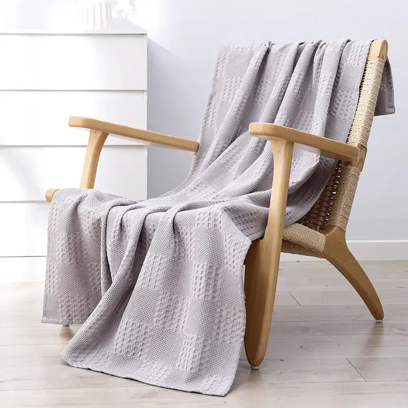 A soft light gray honeycomb waffle cotton throw blanket draped over a wooden wicker chair for bedroom decor