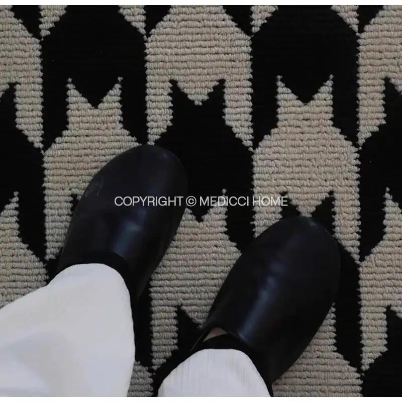 Black glossy leather clogs with rounded toe and low profile design placed on decorbites houndstooth black ivory area rug