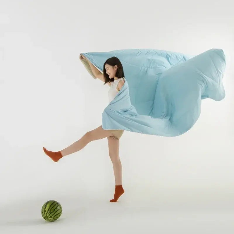 A light blue ice silk cooling blanket billows around a woman in a white bedroom decorbites ice silk comforter