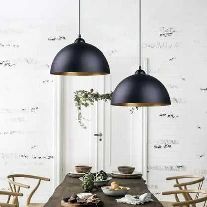 Industrial black and gold metal cage pendant light with black metal cage and gold-trimmed interiors above dining table
