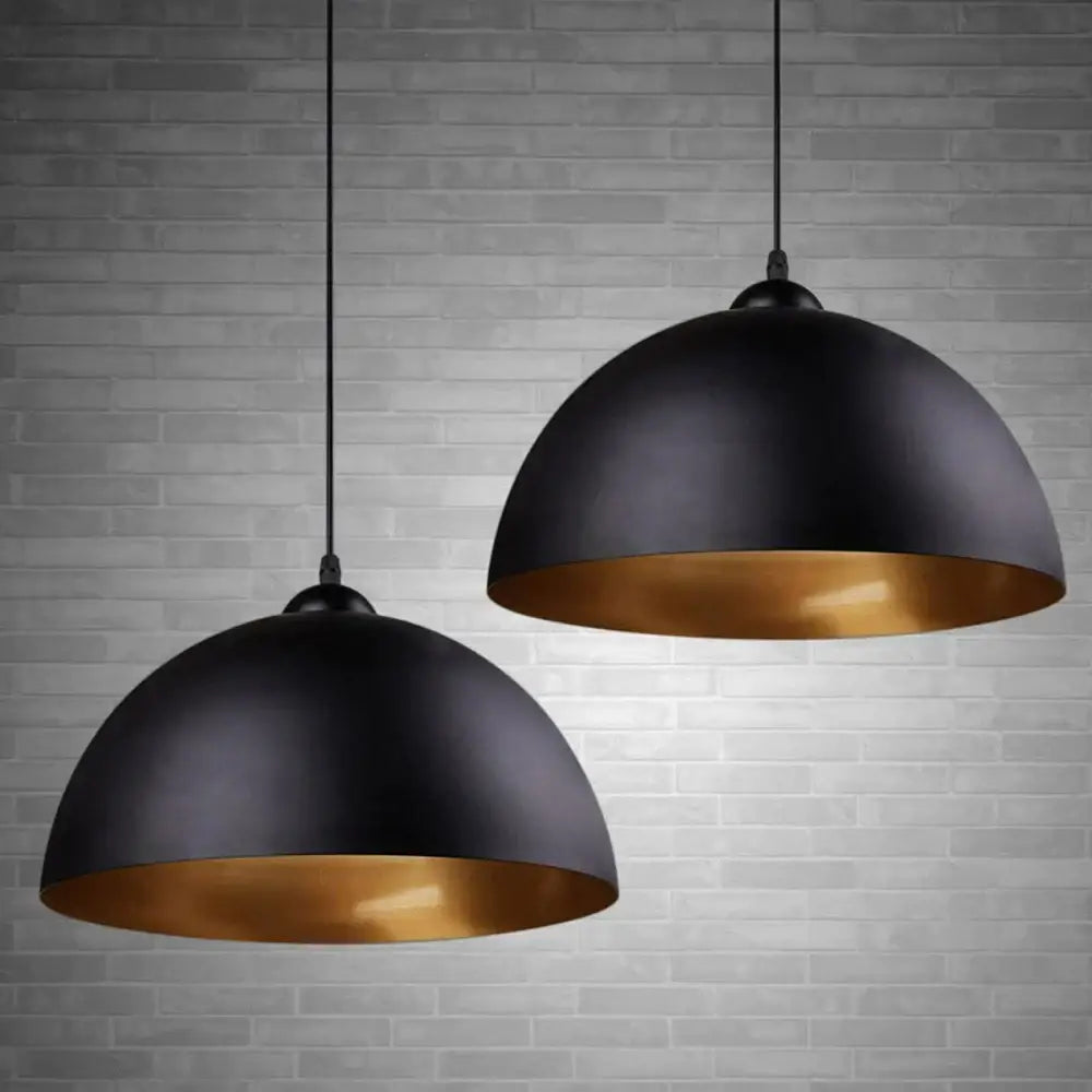 Industrial black and gold metal cage pendant light with black dome and gold-lined interior against gray brick wall