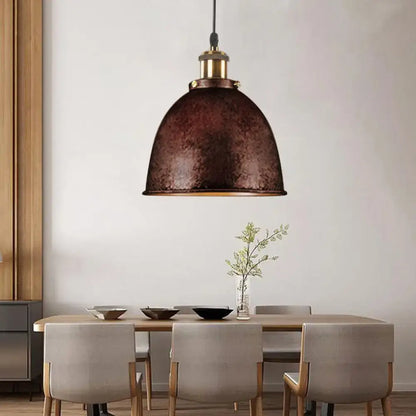 A rustic bronze antique style dome pendant lamp with hammered metal finish and brass hardware above dining table