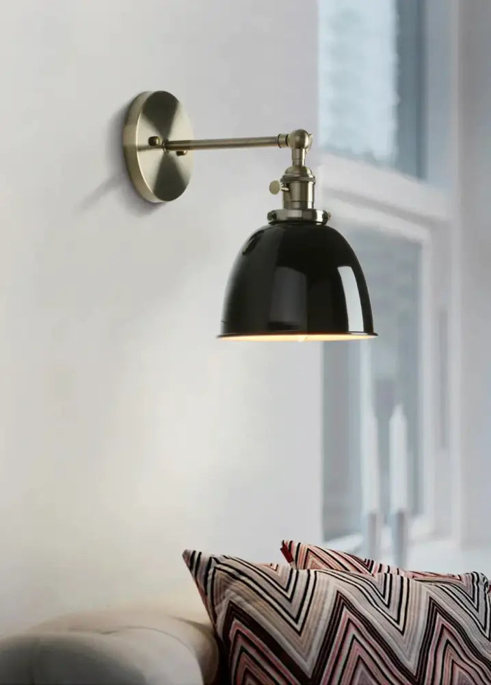 Industrial black wall sconce with black enamel dome and brass-finished metal arms for bedroom lighting