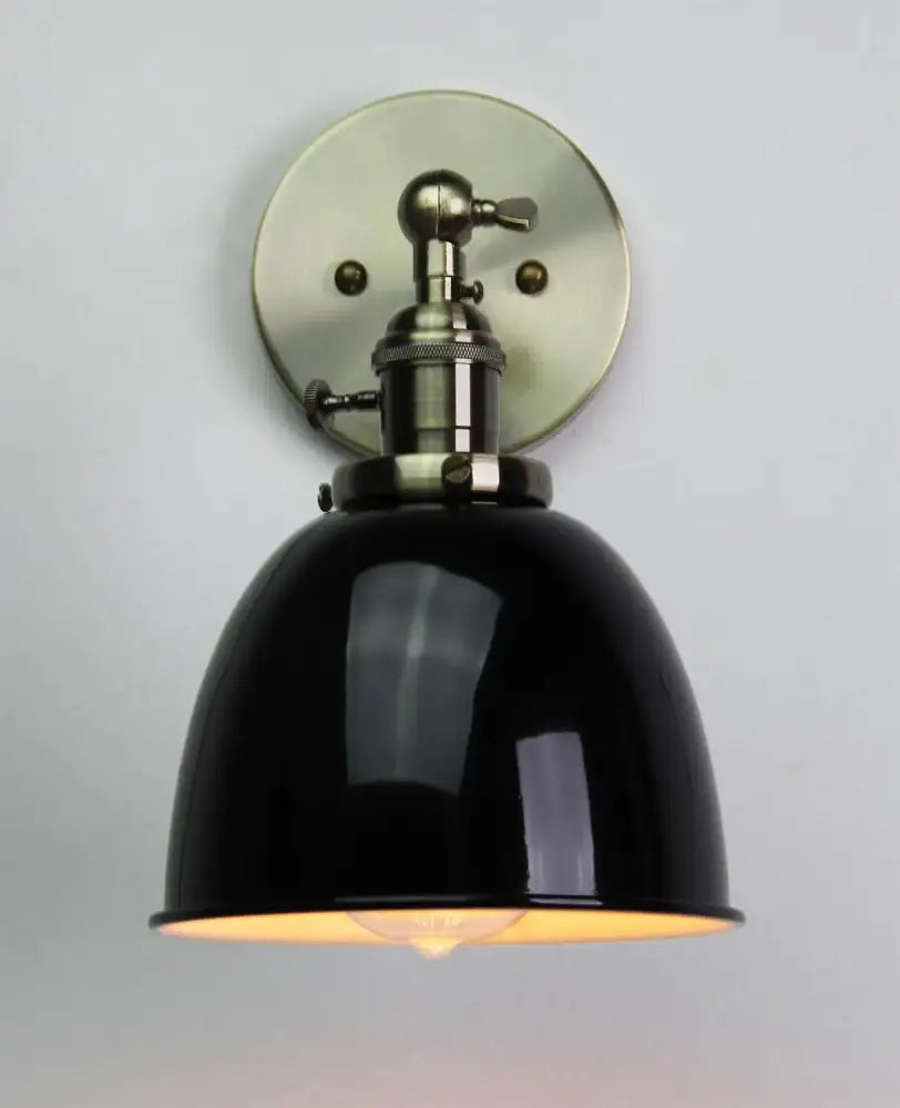 Industrial black wall sconce with black enamel dome shade, adjustable arm, and brushed brass mounting plate for bedroom use