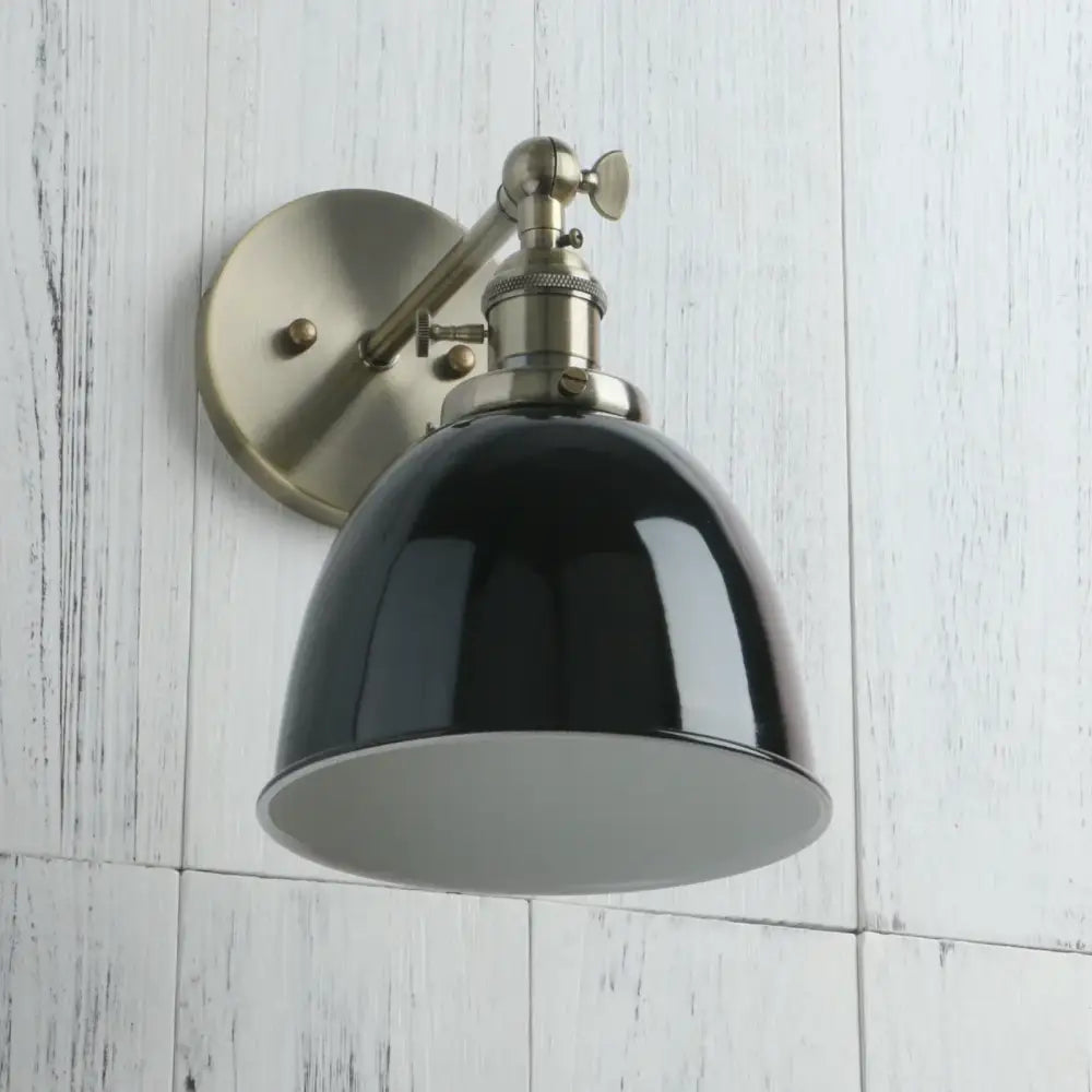 Black wall sconce with enamel dome shade, brushed brass mounting bracket, and adjustable arm for industrial style lighting