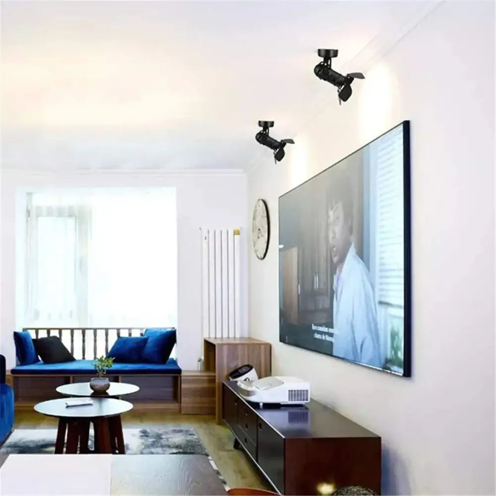 Black-framed flat-screen television on white wall showing industrial black ceiling spotlight lamp with adjustable blades and subtitles