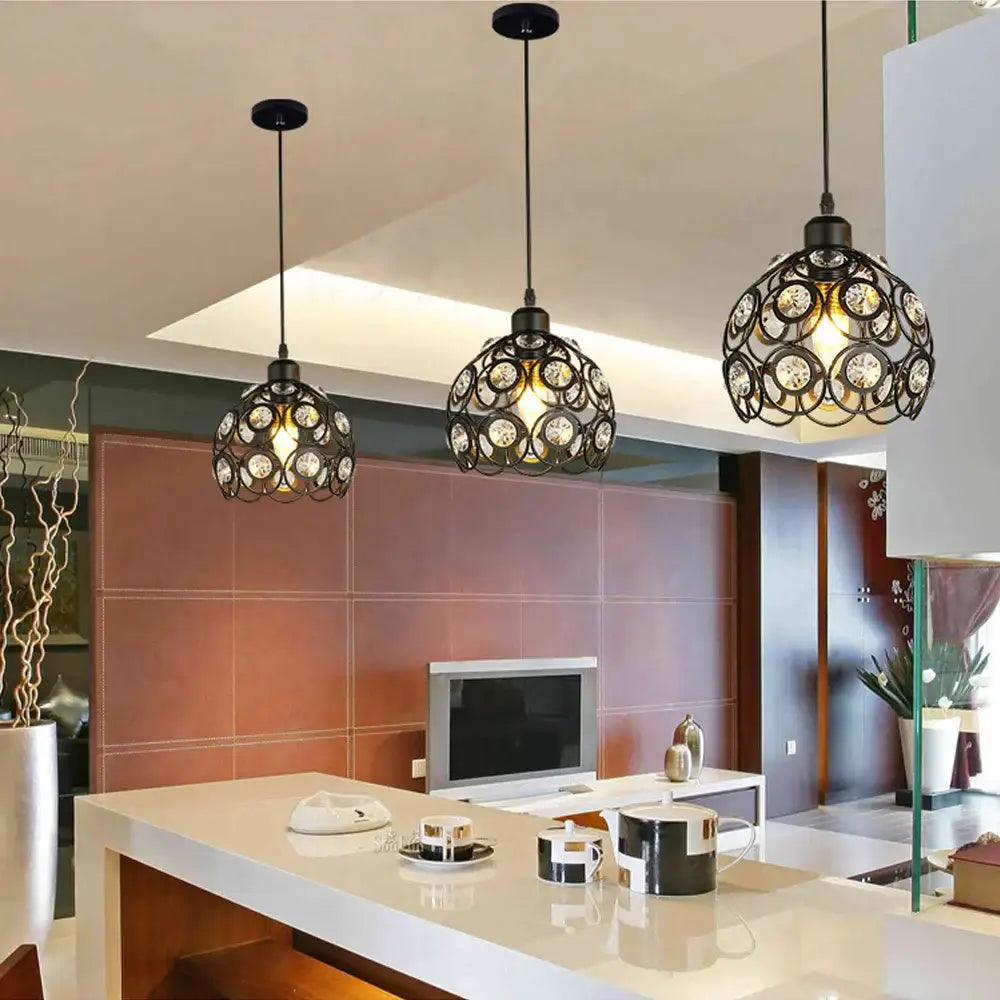 Three black wrought iron industrial crystal k9 pendant lamps with clear crystals hang above a modern kitchen island