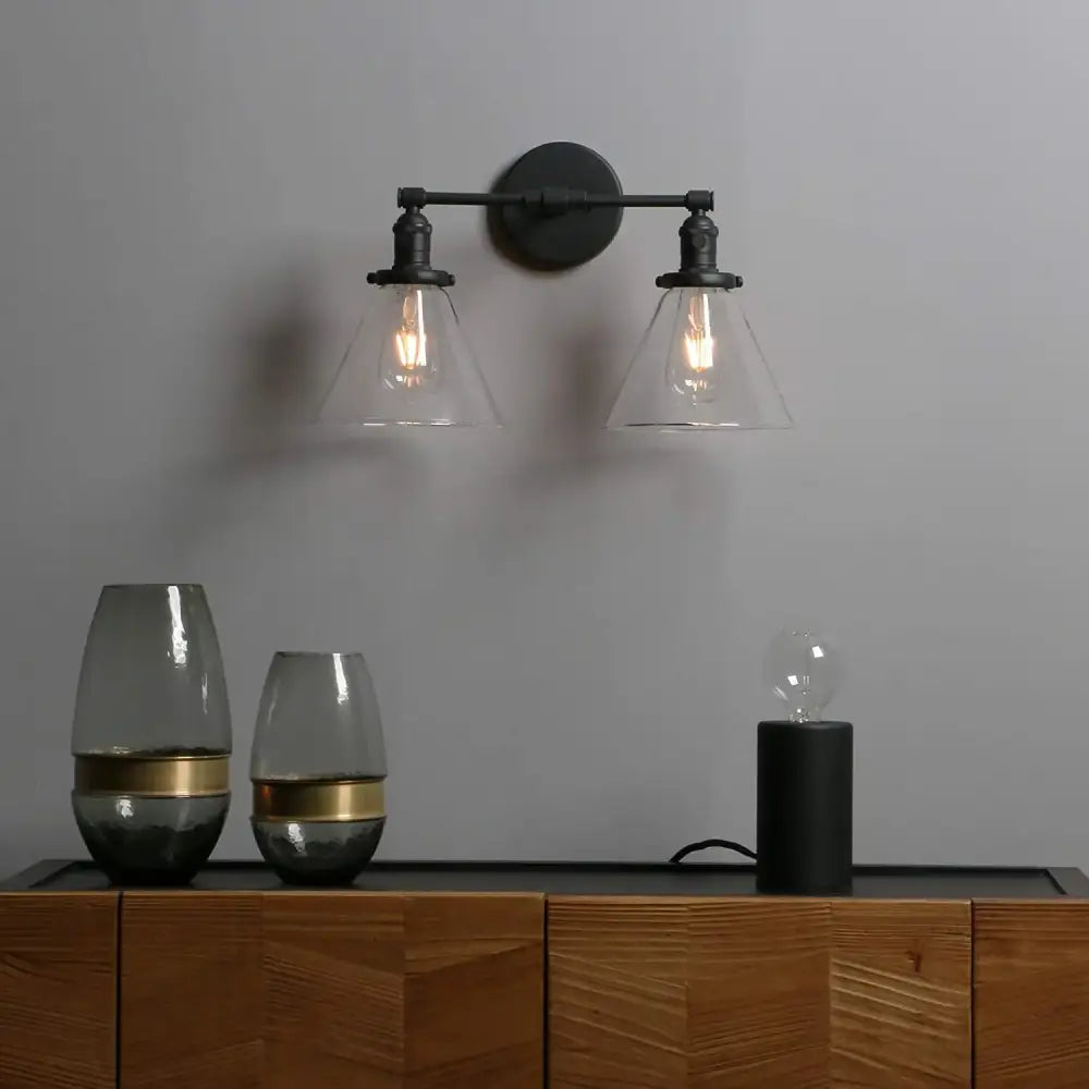 Black wrought iron wall sconce with double cone glass industrial shades and exposed filament bulbs for bedroom lighting
