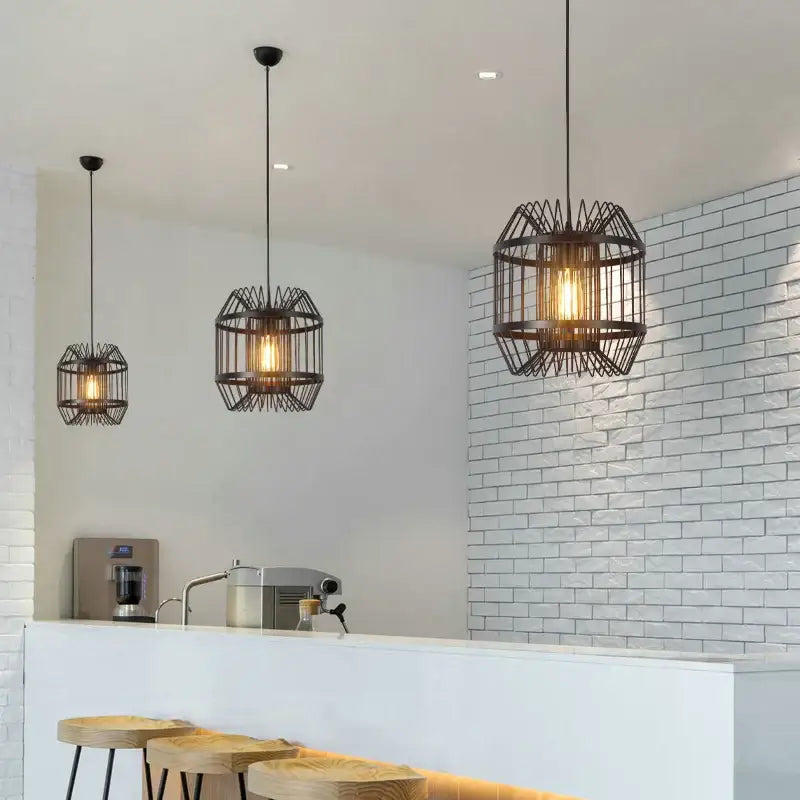 Three black wrought iron industrial pendant light cage frames with warm glowing bulbs for dining room decorbites cage light