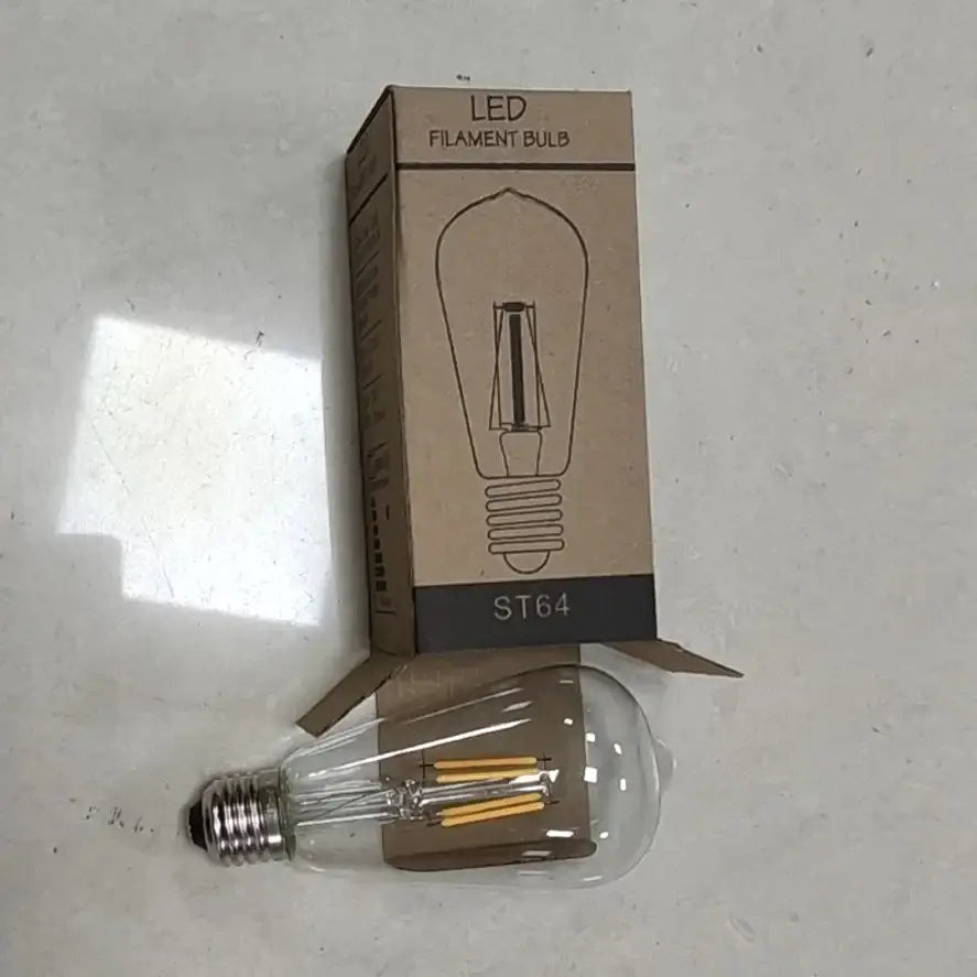 Clear glass led filament bulb with visible yellow filaments and metallic base beside brown packaging for hemp rope wall lamp decorbites