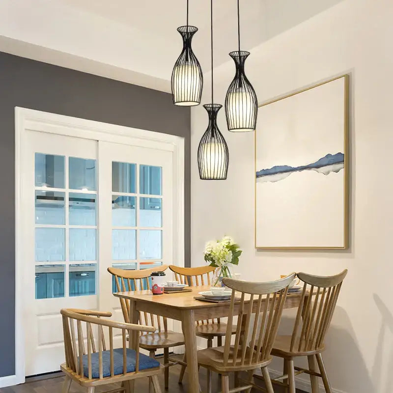 Three black iron cage pendant lights with vertical slats hang above a wooden dining table decorbites iron cage design