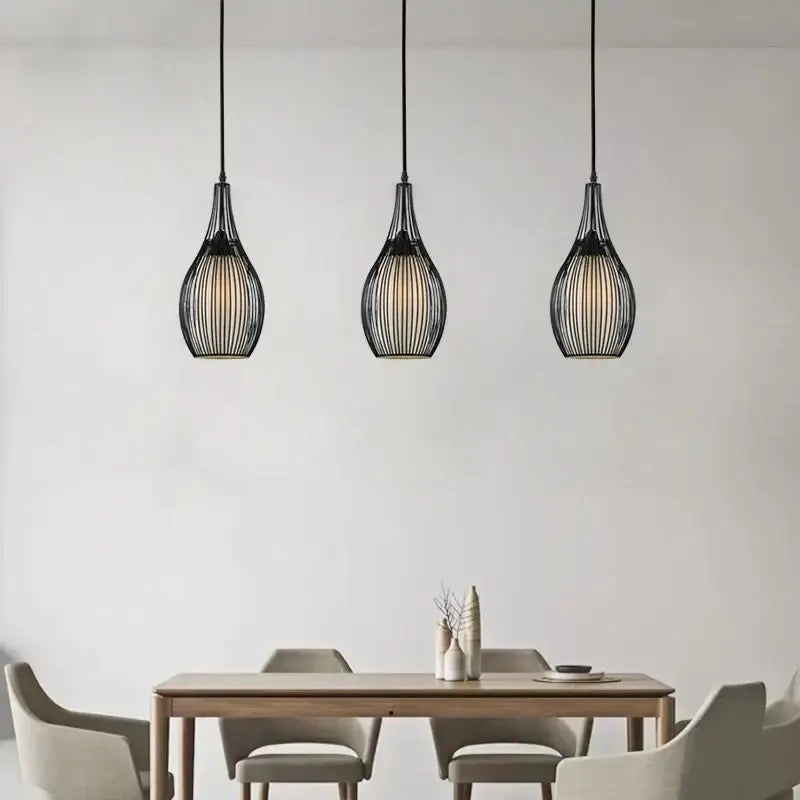 Three black iron cage pendant lights with modern teardrop design from decorbites hang above dining table