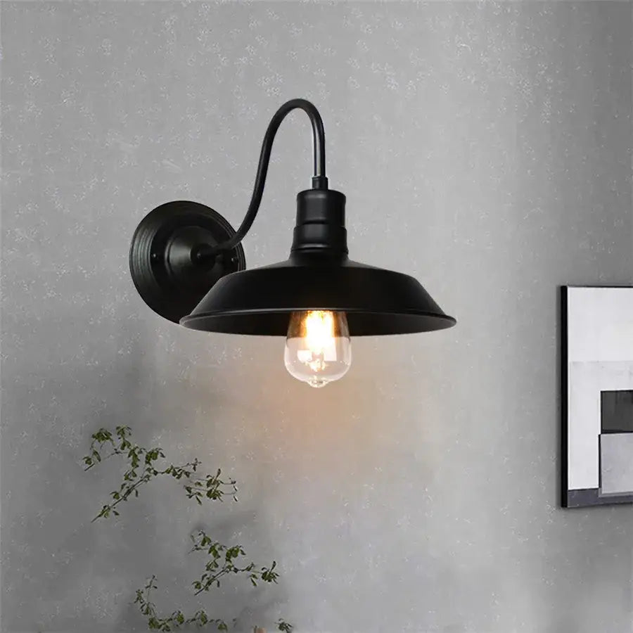 Black wrought iron cage wall sconce with curved arm and wide dome shade housing exposed edison bulb decorbites iron cage