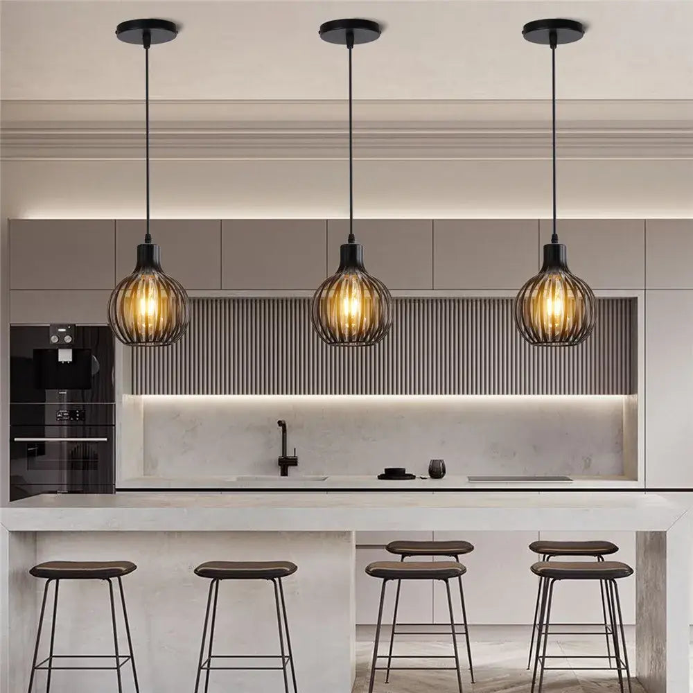 Industrial black metal cage mini pendant light with warm amber bulbs hanging above a modern kitchen island