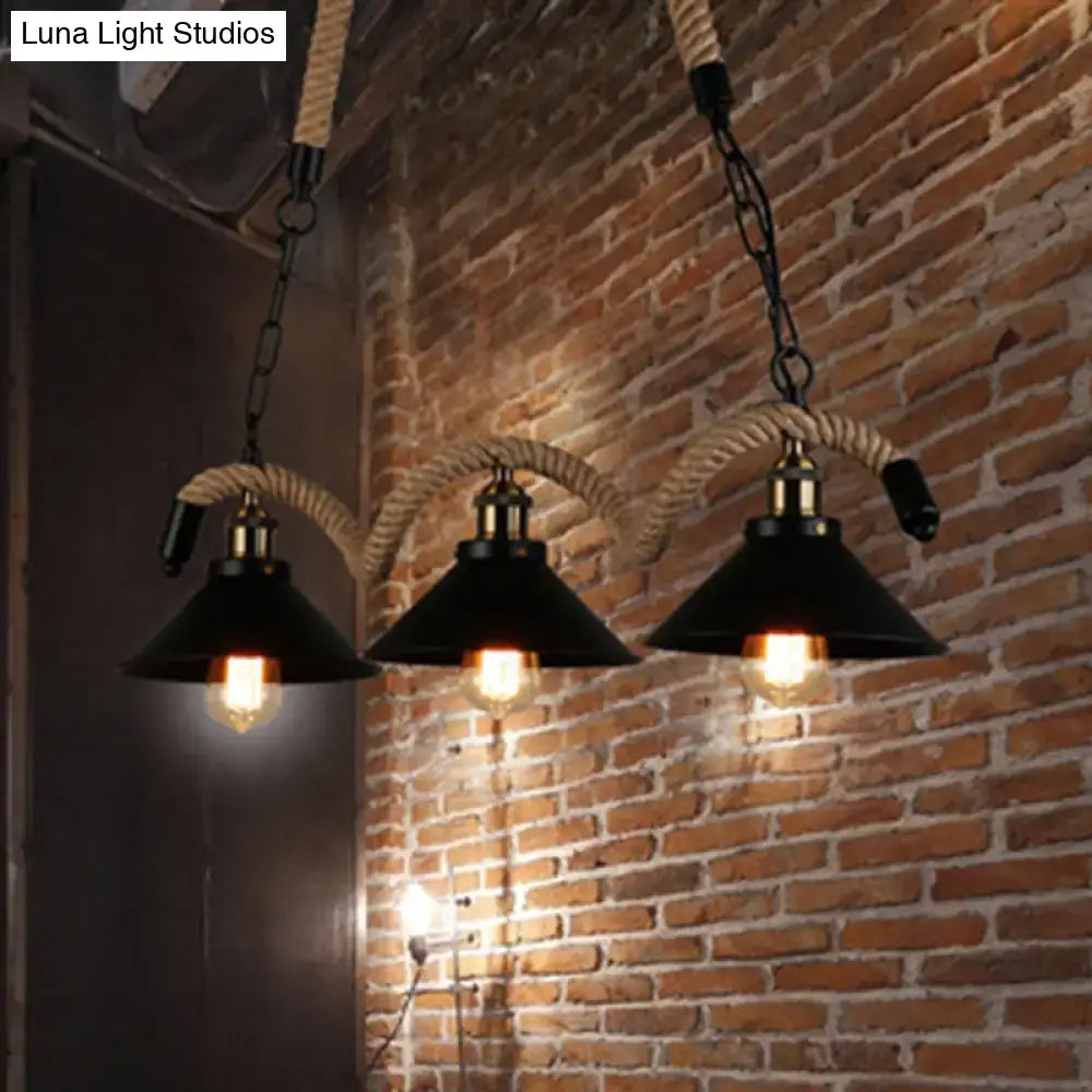 Three black industrial metal island chandelier pendant lights with brass accents and thick rope suspension