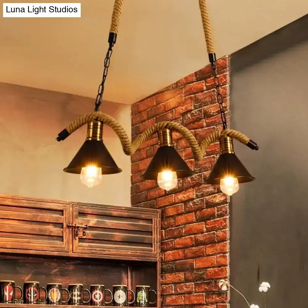 Industrial black metal island chandelier with three black conical shades, brass accents, and rope suspension
