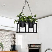 Black metal hanging plant holder with two pots containing green ferns complementing industrial rectangle island light fixture