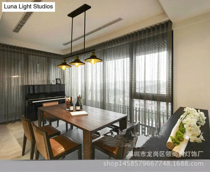 Industrial black metal island pendant with three brass cone shade fixtures hanging above wooden dining table