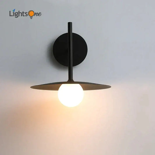 Industrial black minimalist wall lamp with circular base and disc shade featuring a glowing bulb for bedroom style wall