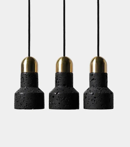 Three black travertine cement pendant lights with gold-toned brass caps hang from thin black cords by decorbites