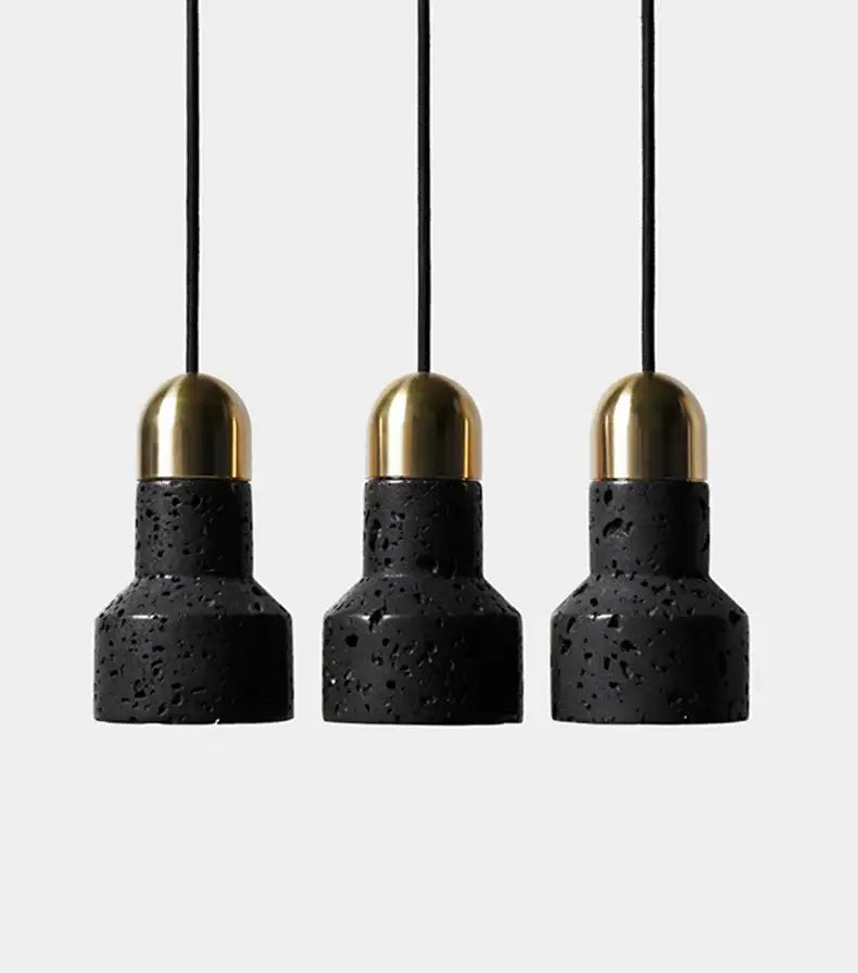 Three black travertine cement pendant lights with gold-toned brass caps hang from thin black cords by decorbites