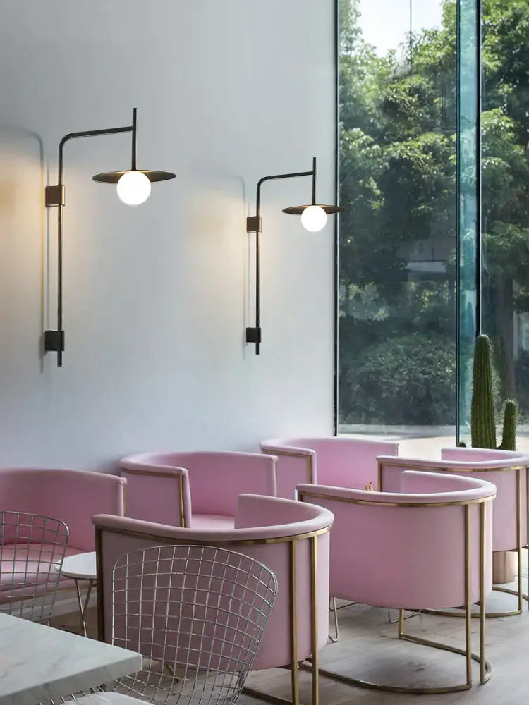 Industrial black wall lamp with minimalist disc sconce complements pink upholstered armchairs with gold metal frames in decorbites industrial style wall setup