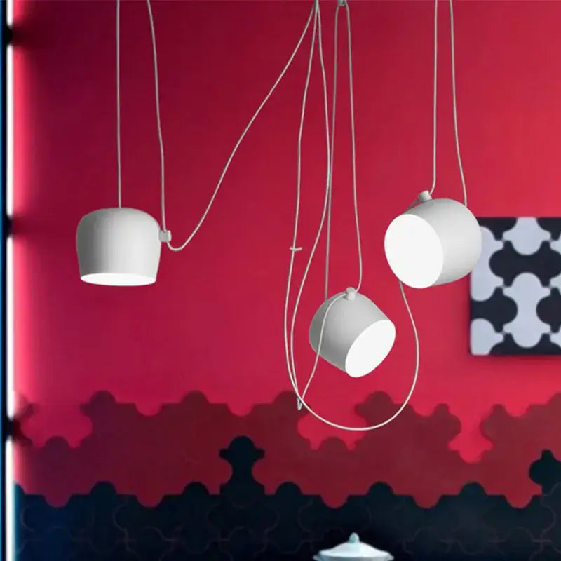 Three white cylindrical pendant lights with curved cords hang against a red wall for decorbites industrial black white dining room decor