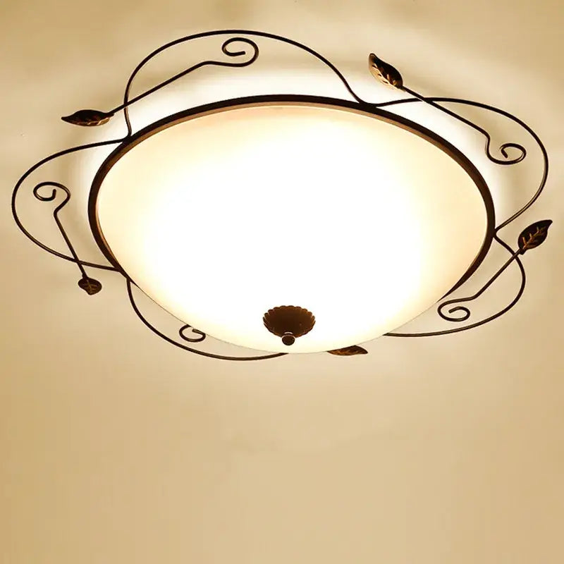 A warm-toned glass round ceiling light with an industrial black wrought iron frame featuring leaf and scroll designs