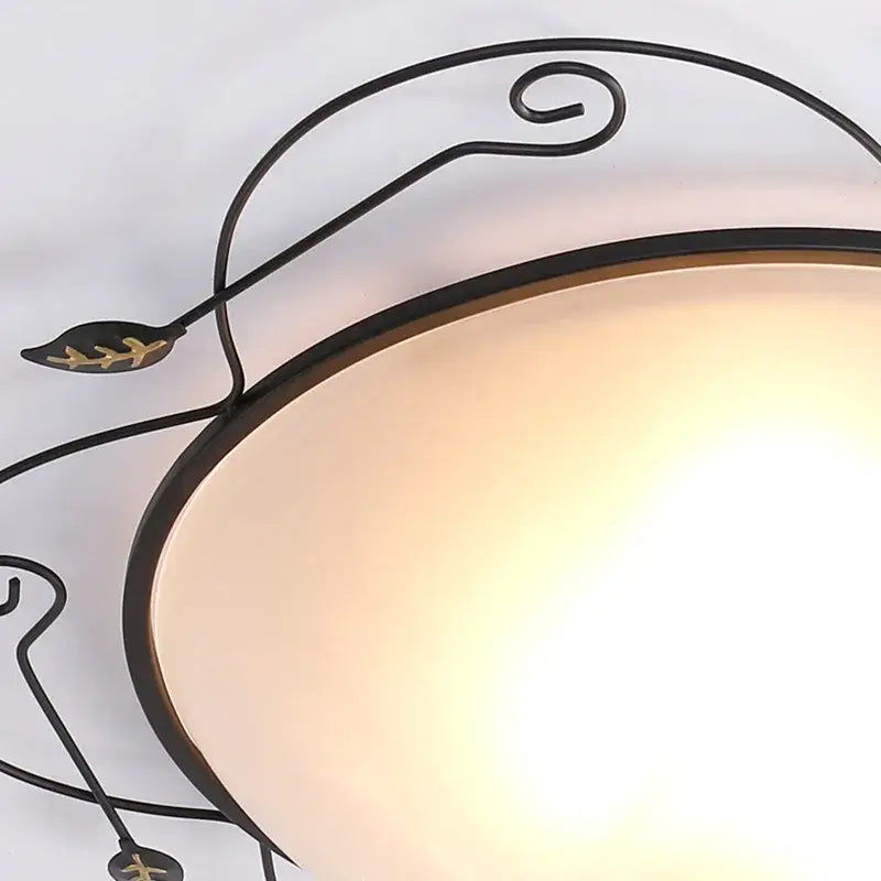 Industrial black wrought iron round ceiling light with ornate leaf designs and warm-toned glass round ceiling diffuser