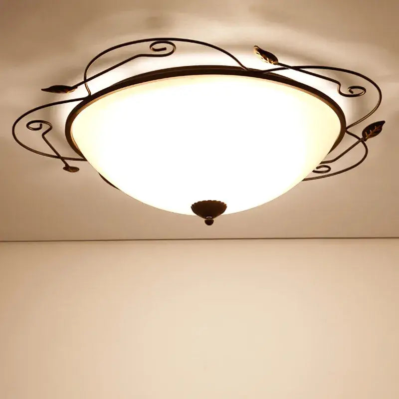 Industrial black wrought iron round ceiling light with a warm glass round ceiling and ornate leaf scroll design