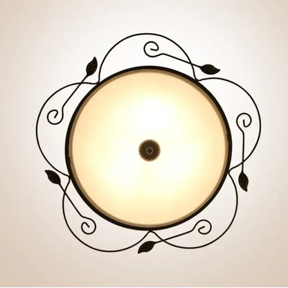 Industrial black wrought iron round ceiling light with ornate leaf designs and warm glass round ceiling shade