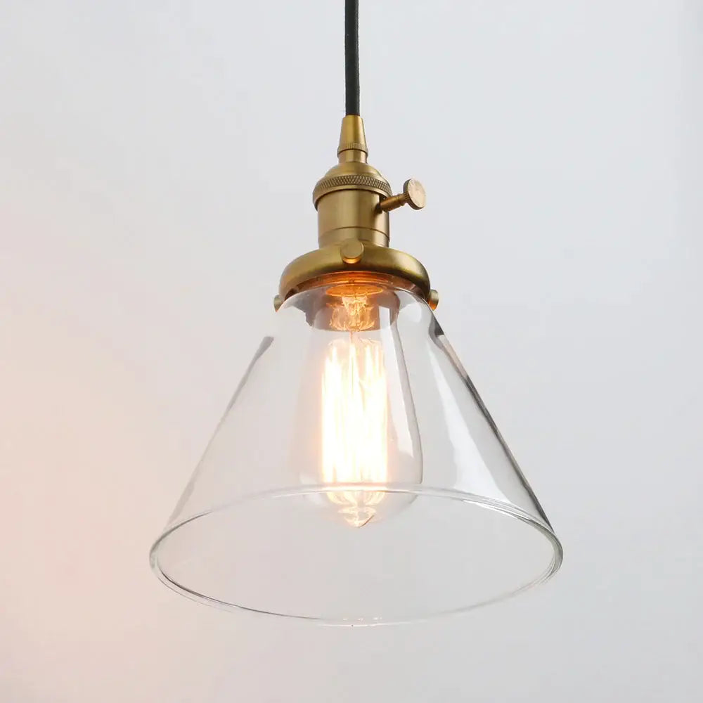 A clear funnel flared glass pendant light with brass industrial fixture and exposed filament bulb for kitchen decorbites