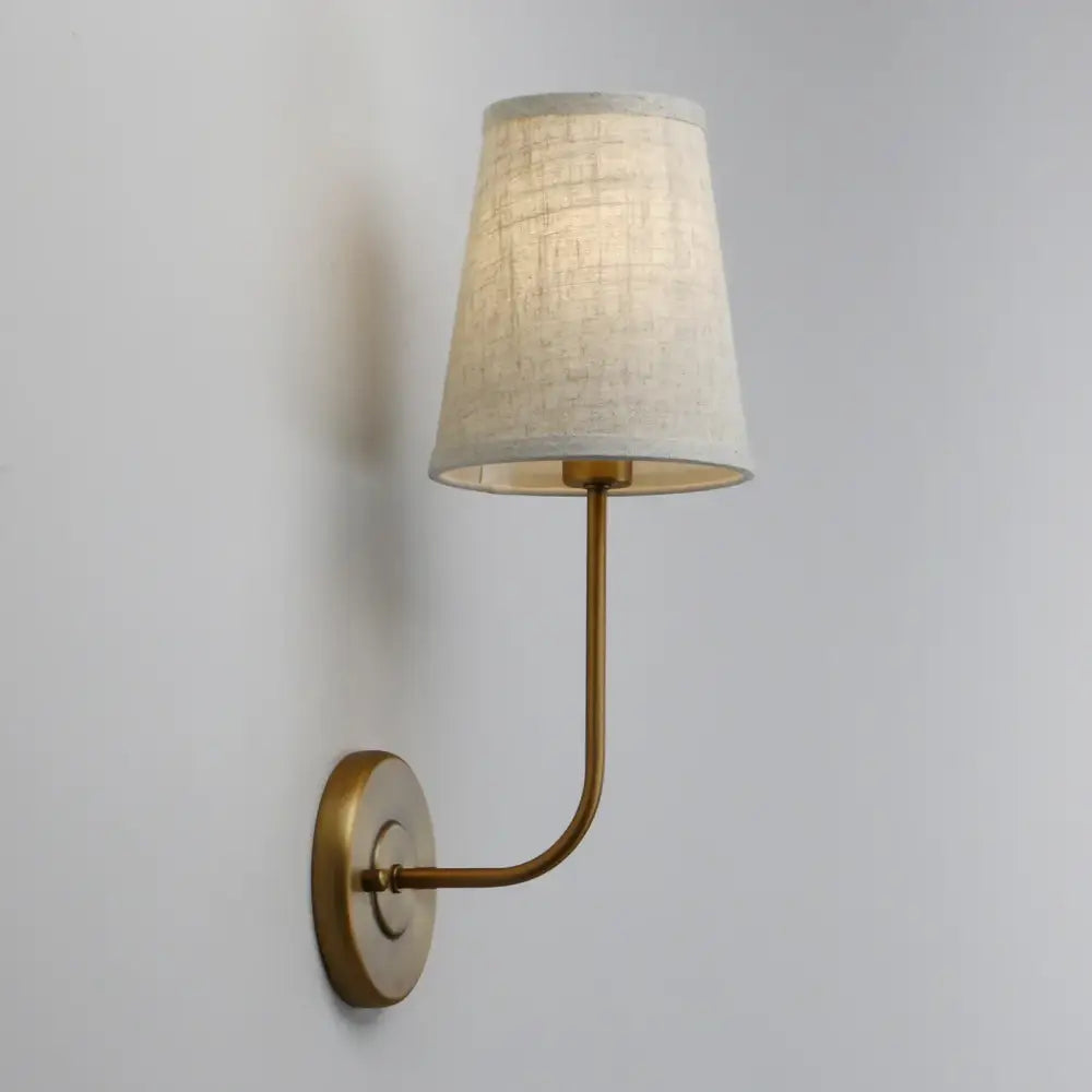 Industrial brass wall lamp set featuring a brass-finished sconce with a curved arm and off-white linen shade for reading