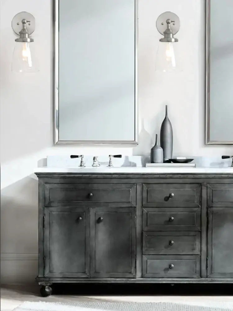 Dark gray distressed wood bathroom vanity with silver hardware and white countertop beside industrial brushed nickel clear glass wall lamp decorbites clear glass