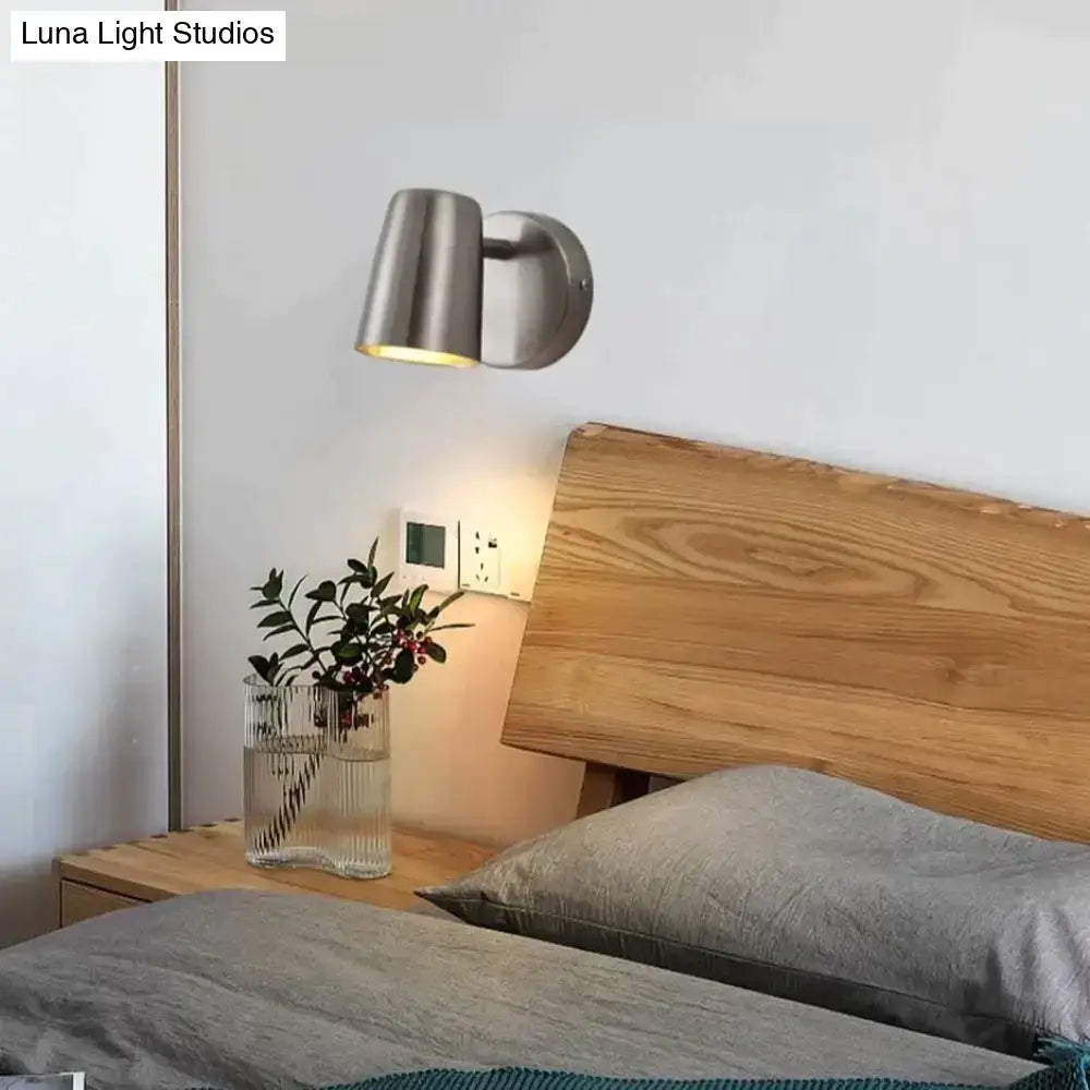 Modern industrial led wall sconce in brushed nickel with a cylindrical lamp head and circular mounting plate for bedroom use