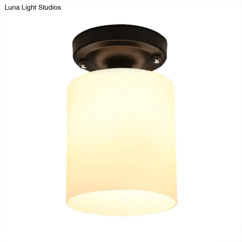 Warm-toned cylindrical industrial milky glass shade on a black semi flush light with dark bronze ceiling mount for corridor
