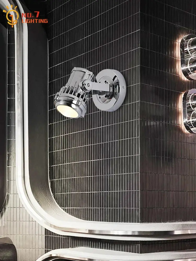 Industrial chrome adjustable wall lamp with sleek spotlight head mounted on dark tiled wall for bedroom lighting