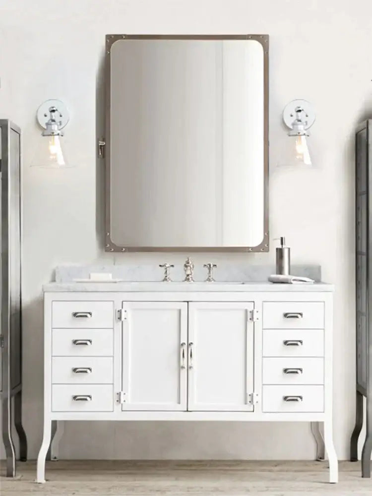 White vanity with silver hardware and marble countertop illuminated by industrial chrome glass shade wall sconce light fixture