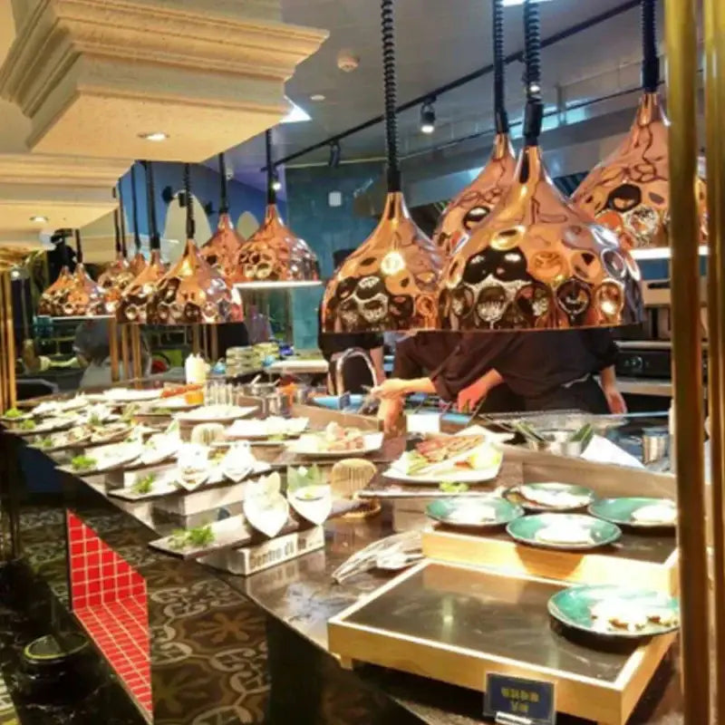 Copper-colored industrial electric food heat pendant lights with black spiral cords hanging above buffet counter
