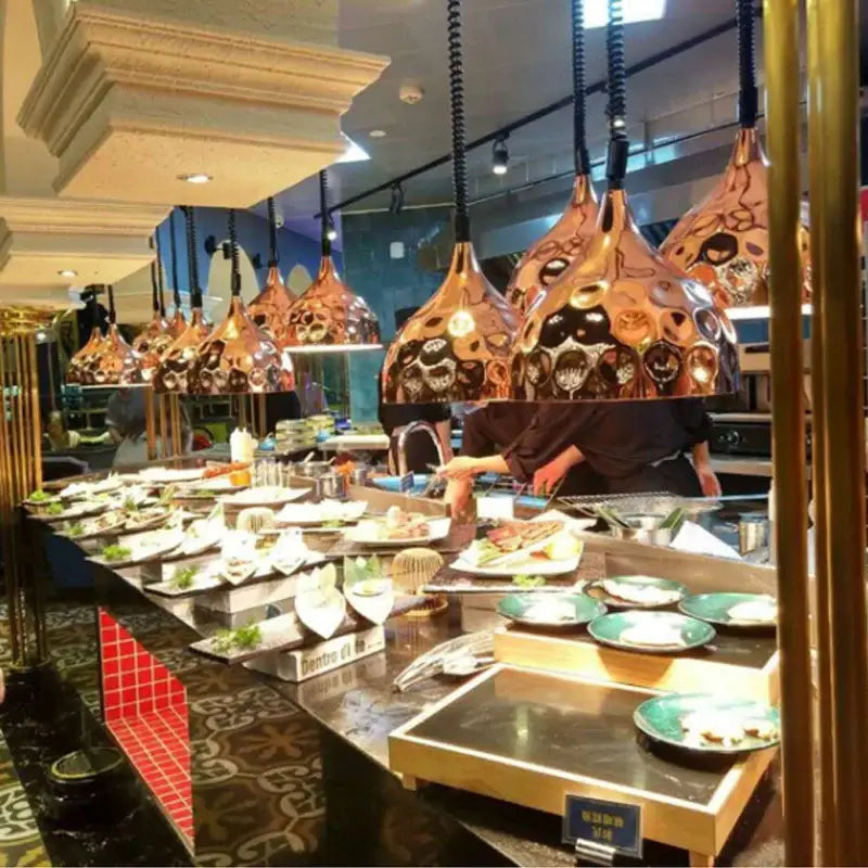 Copper-colored industrial electric heat lamp pendant lights with intricate black and gold patterns above buffet counter