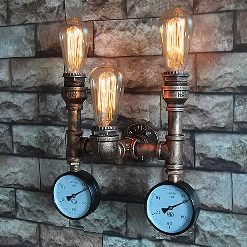 Industrial dark brass pipe wall lights with three glowing filament bulbs and two pressure gauges on brick background