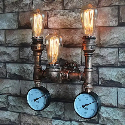 Industrial dark brass pipe wall lights with three glowing filament bulbs and two pressure gauges on rustic brick wall