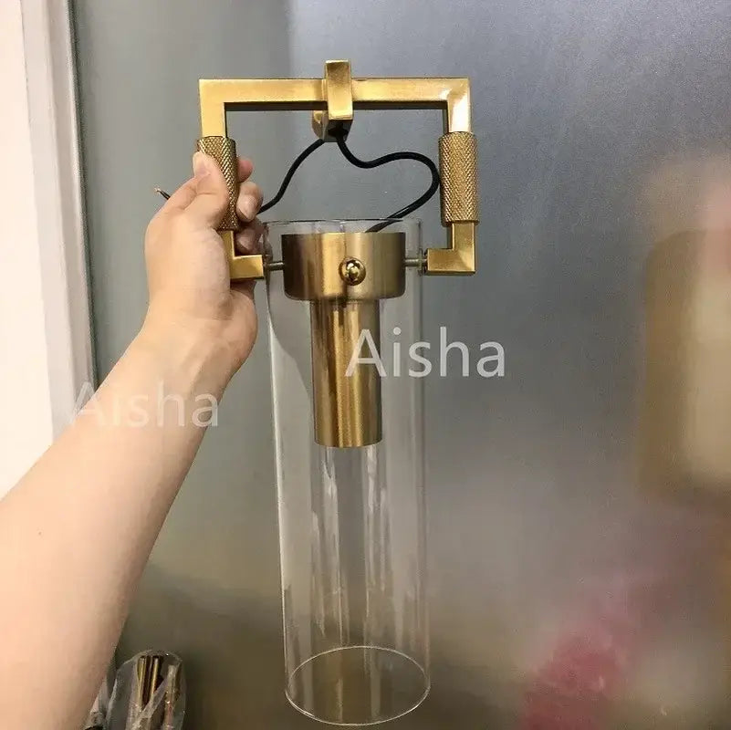 A modern industrial glass wall lamp with brass frame, clear glass cylinder, and textured gold knobs for bedroom decorbites industrial glass